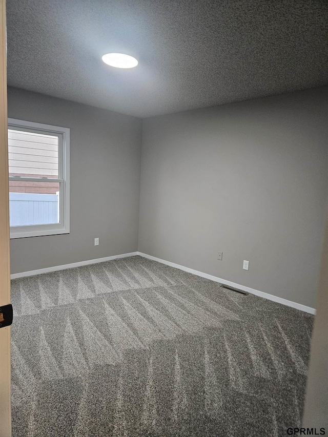 empty room with carpet, visible vents, baseboards, and a textured ceiling