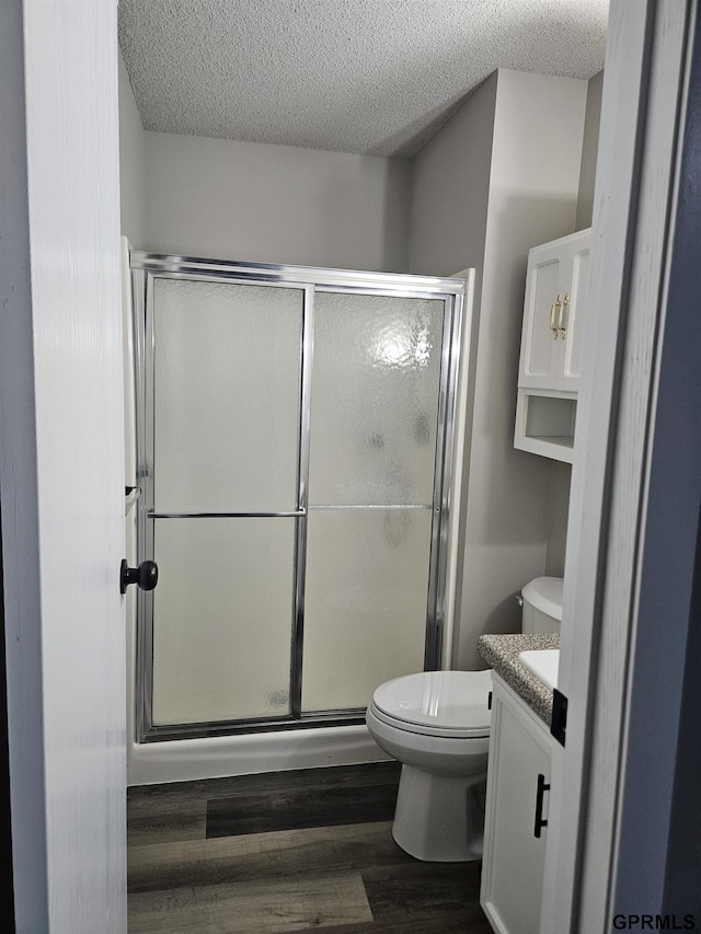 full bathroom with a textured ceiling, a stall shower, wood finished floors, and toilet