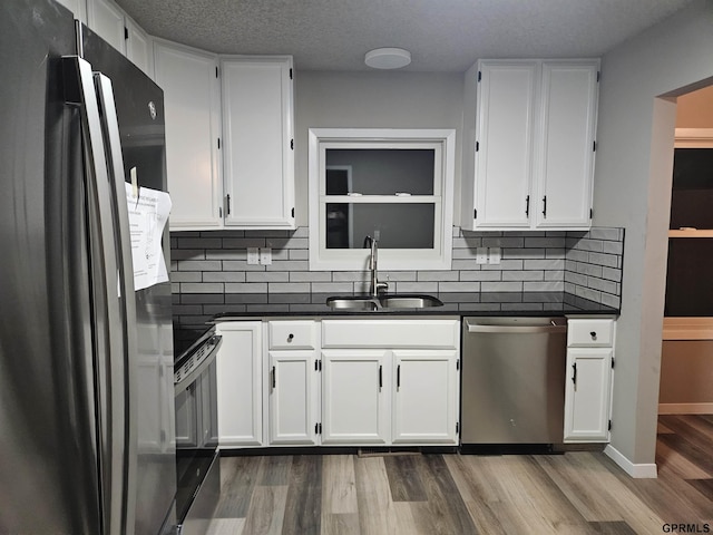 kitchen featuring wood finished floors, appliances with stainless steel finishes, dark countertops, and a sink