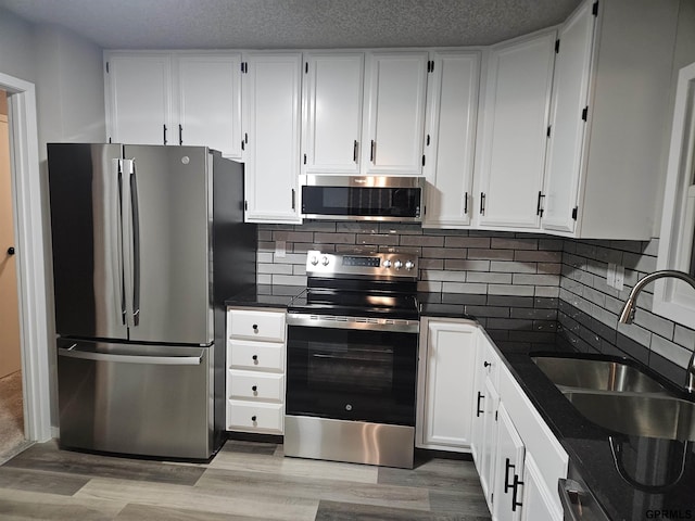 kitchen with light wood-style floors, appliances with stainless steel finishes, white cabinets, and a sink