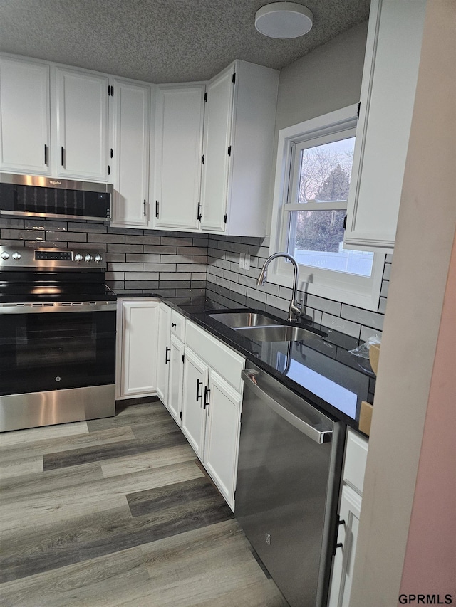 kitchen featuring tasteful backsplash, dark countertops, appliances with stainless steel finishes, white cabinetry, and a sink