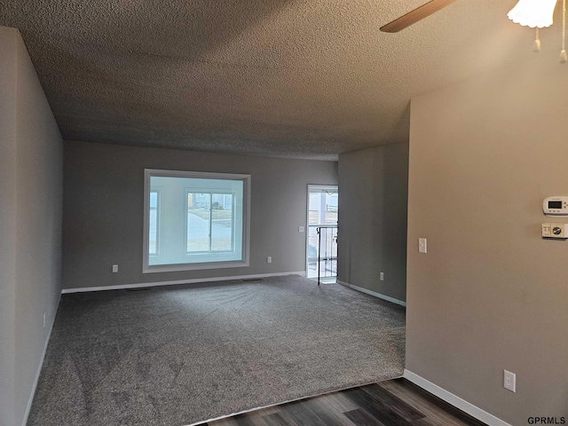 empty room featuring a textured ceiling, ceiling fan, dark wood-style flooring, and baseboards