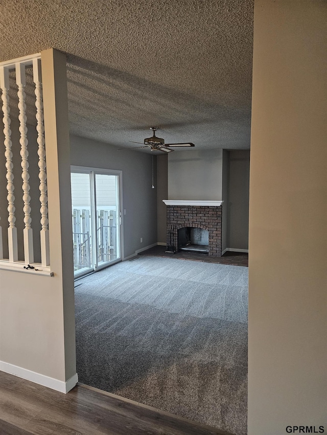 unfurnished living room featuring a brick fireplace, ceiling fan, baseboards, and a textured ceiling