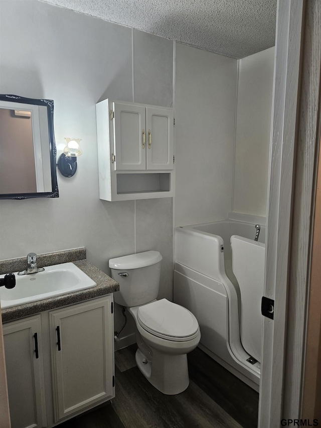 full bathroom with a textured ceiling, a washtub, toilet, wood finished floors, and vanity