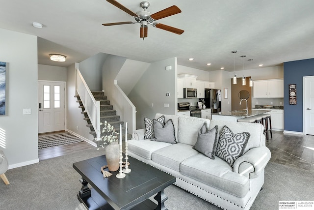 living area featuring a ceiling fan, recessed lighting, dark colored carpet, baseboards, and stairs