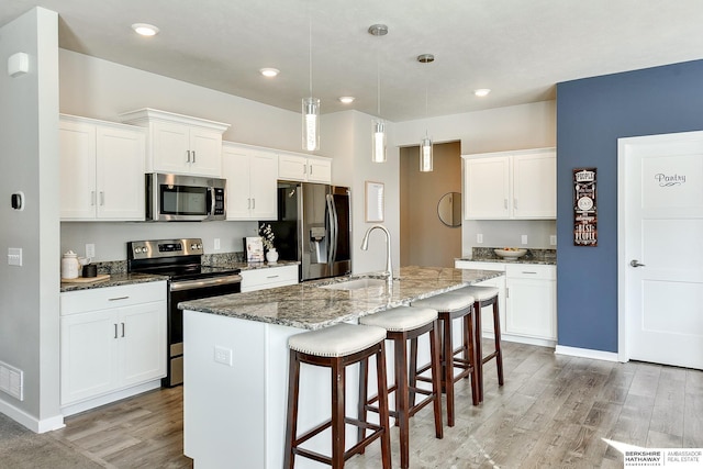 kitchen with light wood finished floors, stainless steel appliances, a kitchen bar, and a sink