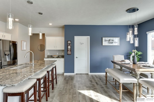 kitchen with a kitchen bar, stainless steel refrigerator with ice dispenser, wood finished floors, white cabinets, and a sink