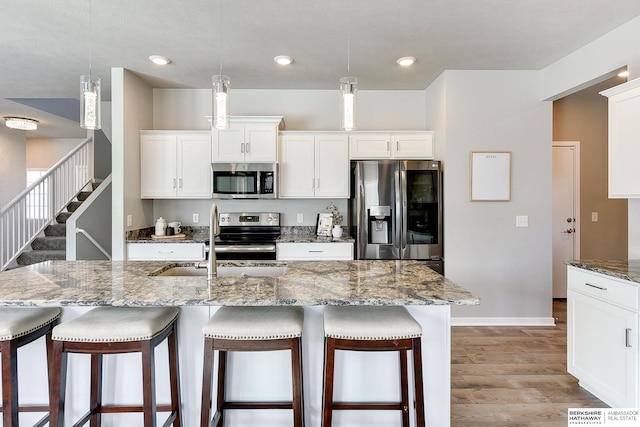 kitchen featuring a breakfast bar, light stone counters, appliances with stainless steel finishes, wood finished floors, and a sink