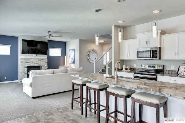 kitchen with a breakfast bar area, stone counters, a sink, a stone fireplace, and stainless steel appliances