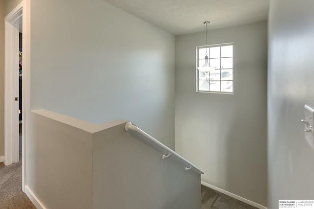 hall with an upstairs landing, dark colored carpet, and baseboards