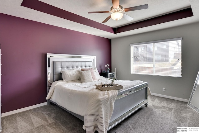 carpeted bedroom with a tray ceiling, baseboards, and a ceiling fan