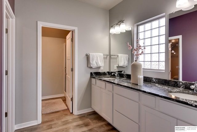 full bath featuring double vanity, wood finished floors, baseboards, and a sink