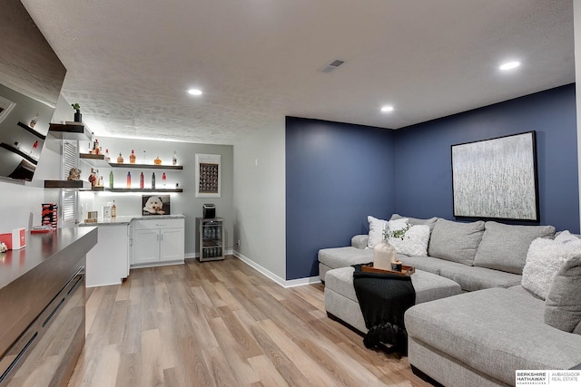 living room with beverage cooler, visible vents, baseboards, light wood-style flooring, and a bar