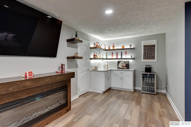 bar featuring light wood-style floors, wine cooler, bar area, and a textured ceiling