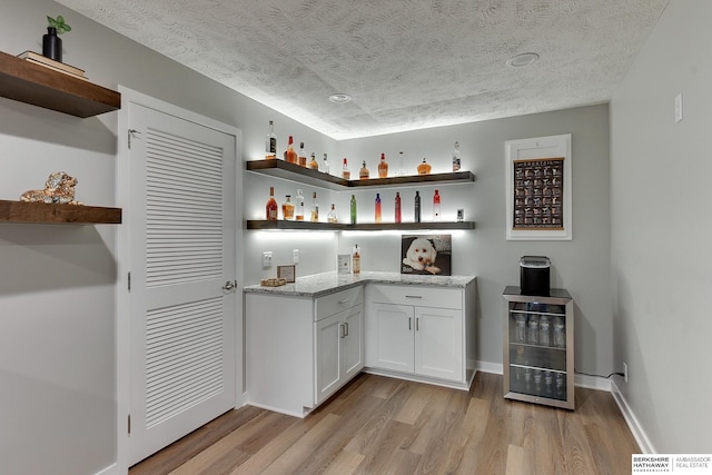 bar with beverage cooler, baseboards, light wood-style flooring, a textured ceiling, and a dry bar