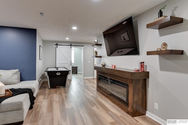 living room with a barn door, light wood-style flooring, baseboards, and visible vents