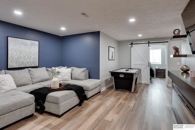 living room with light wood finished floors, visible vents, baseboards, a barn door, and recessed lighting