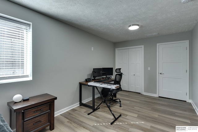 office space with visible vents, baseboards, light wood finished floors, and a textured ceiling