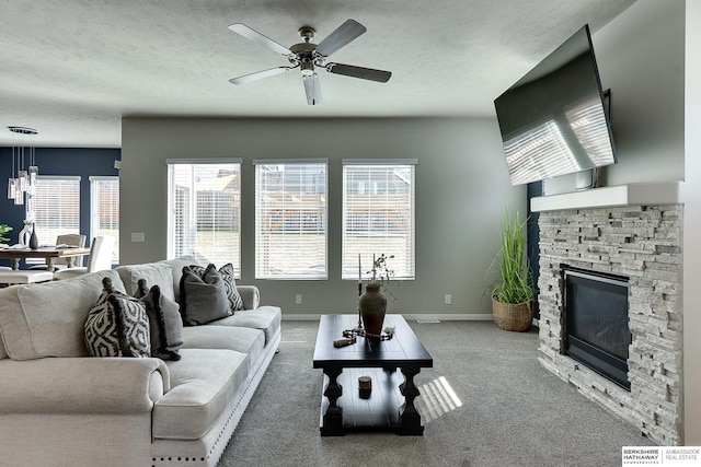 living area with carpet flooring, a textured ceiling, a stone fireplace, and baseboards