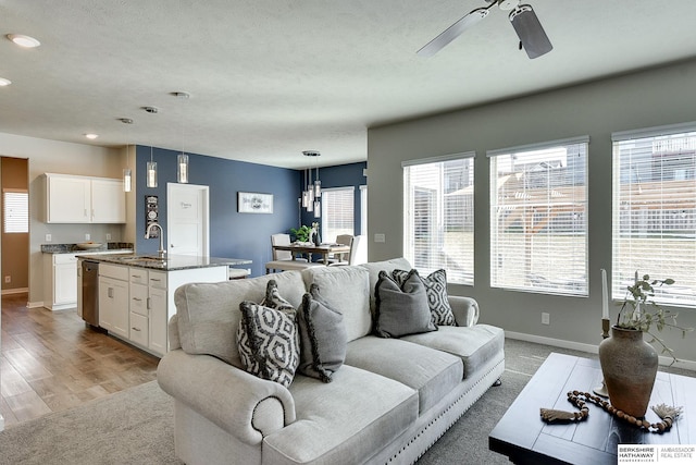 living area featuring plenty of natural light, a ceiling fan, baseboards, and light wood finished floors