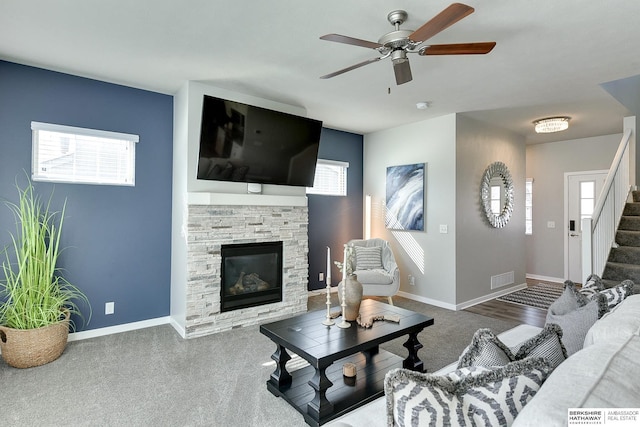 living room featuring a wealth of natural light, stairway, a stone fireplace, and baseboards