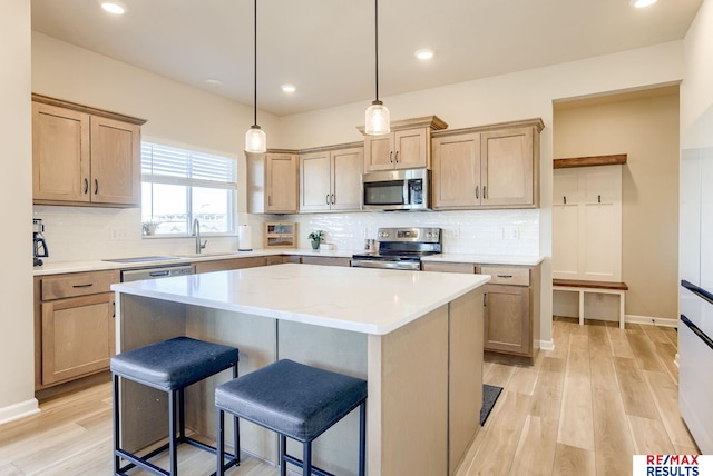 kitchen featuring light wood-style flooring, a sink, stainless steel appliances, a kitchen bar, and a center island