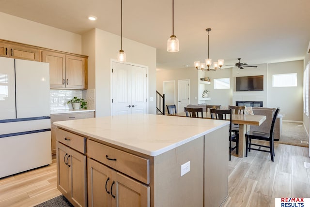 kitchen with light wood-type flooring, freestanding refrigerator, a glass covered fireplace, decorative light fixtures, and tasteful backsplash