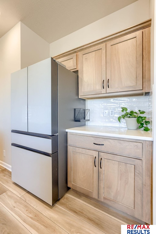 kitchen featuring light wood-style flooring, light brown cabinetry, backsplash, freestanding refrigerator, and light countertops