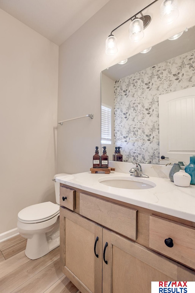 bathroom with toilet, wood finished floors, vanity, and wallpapered walls