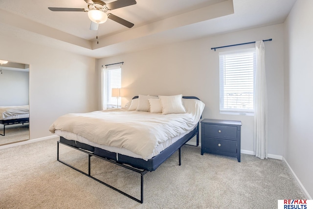 bedroom featuring a tray ceiling, light carpet, and baseboards