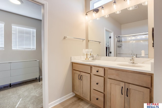 full bath featuring double vanity, a stall shower, baseboards, and a sink