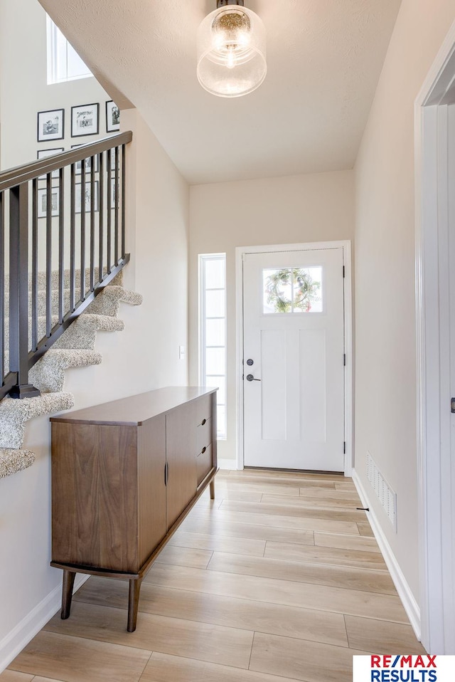 entryway featuring stairs, baseboards, visible vents, and light wood-type flooring