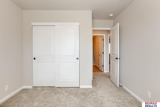 unfurnished bedroom featuring light carpet, baseboards, and a closet