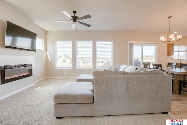 living room with a tiled fireplace, ceiling fan with notable chandelier, baseboards, and light carpet