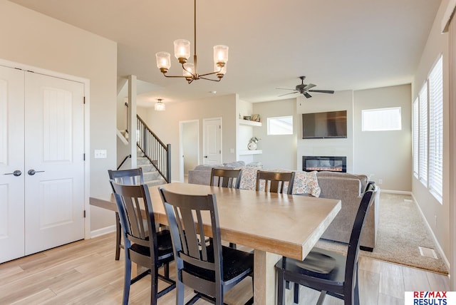 dining space featuring a glass covered fireplace, stairs, ceiling fan with notable chandelier, and light wood-type flooring