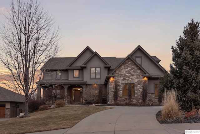 craftsman-style house with stone siding, a front yard, concrete driveway, and stucco siding