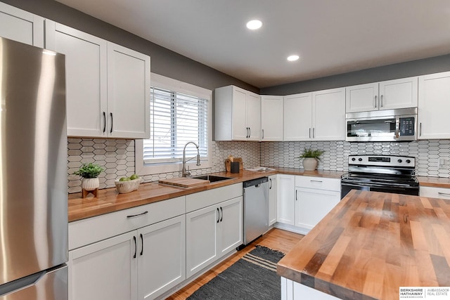 kitchen featuring decorative backsplash, wood counters, appliances with stainless steel finishes, white cabinetry, and a sink