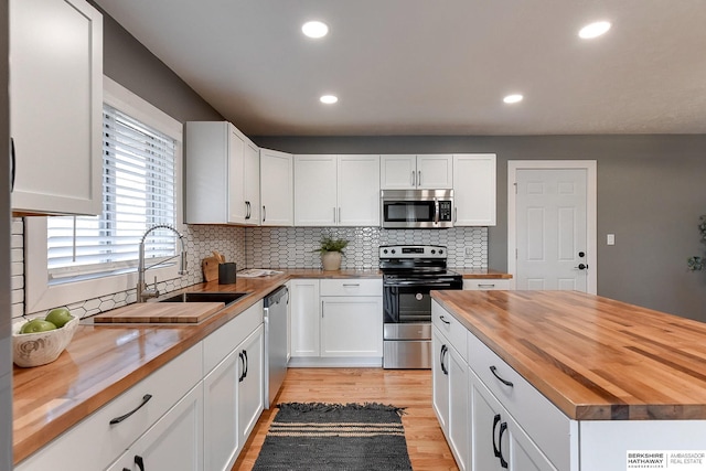 kitchen with butcher block counters, light wood-style flooring, backsplash, appliances with stainless steel finishes, and a sink