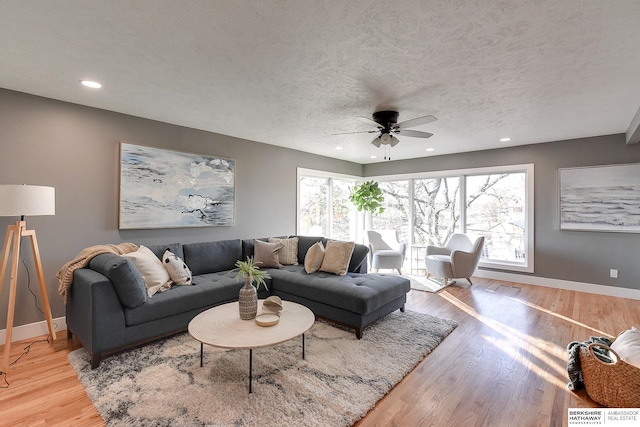 living room featuring a textured ceiling, ceiling fan, light wood-type flooring, and baseboards