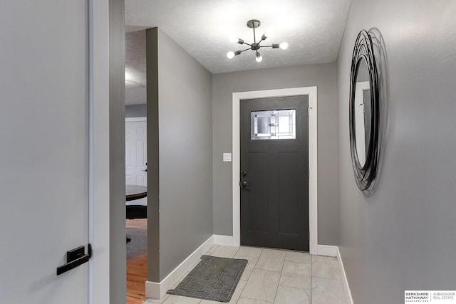 foyer featuring a chandelier, a textured ceiling, and baseboards