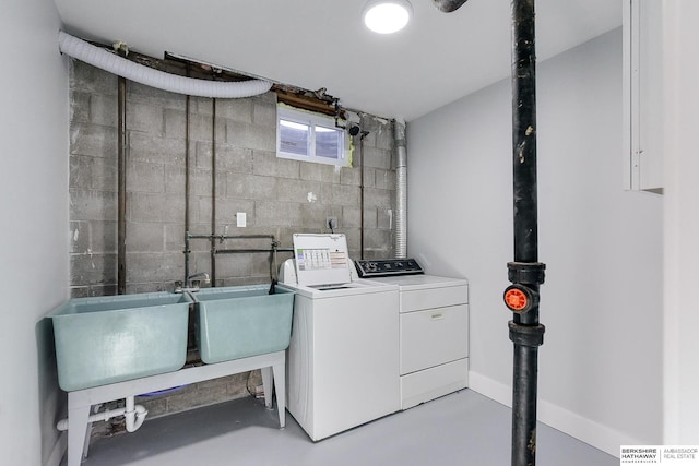 clothes washing area with concrete block wall, washer and clothes dryer, a sink, laundry area, and baseboards