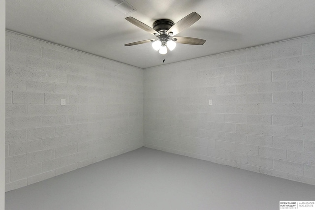 spare room featuring concrete block wall, ceiling fan, and finished concrete floors