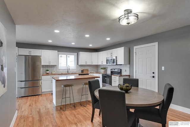 dining area featuring light wood-style floors, recessed lighting, a textured ceiling, and baseboards