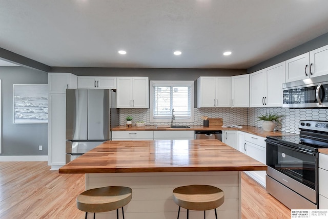 kitchen featuring a kitchen bar, appliances with stainless steel finishes, wooden counters, and a sink