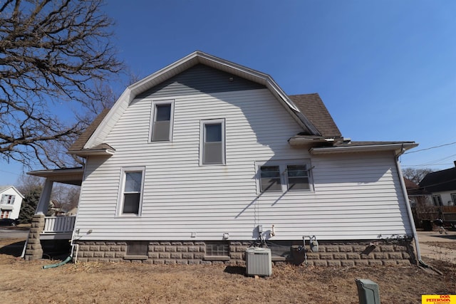 view of side of home with central AC unit, a gambrel roof, and roof with shingles