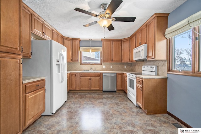 kitchen featuring white appliances, a sink, light countertops, backsplash, and brown cabinetry