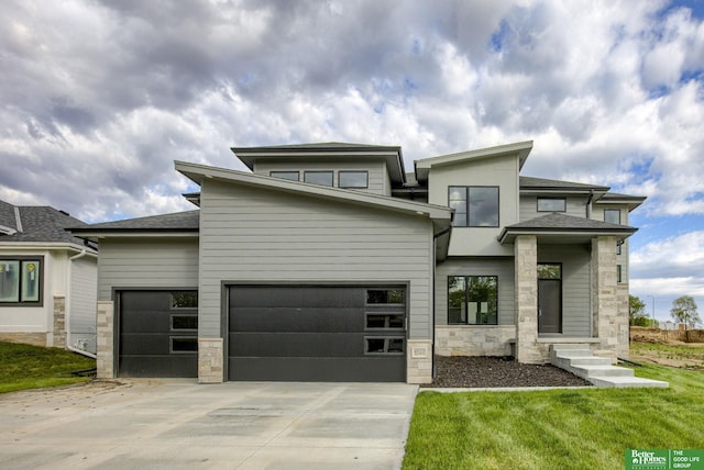 view of front facade featuring a shingled roof, a garage, stone siding, driveway, and a front lawn