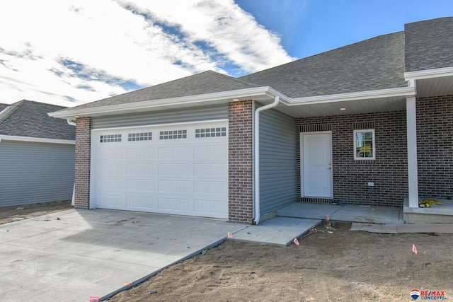 exterior space with a shingled roof, concrete driveway, brick siding, and a garage