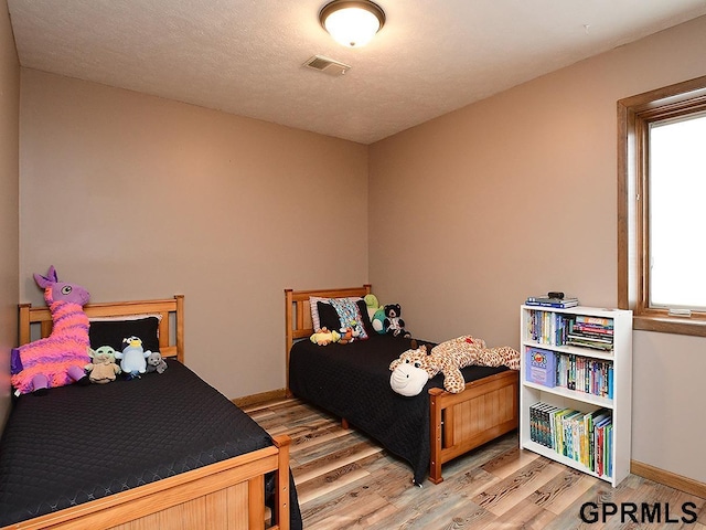 bedroom with a textured ceiling, wood finished floors, visible vents, and baseboards