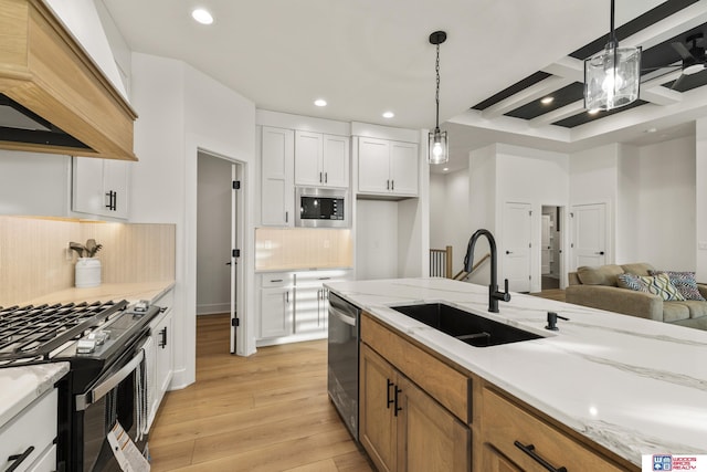 kitchen featuring light wood finished floors, stainless steel appliances, custom range hood, hanging light fixtures, and a sink